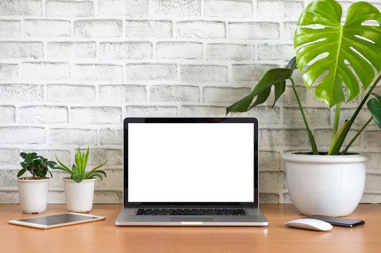 Blank screen of Laptop computer with tablet, mobile phone, mouse and monstera plant pots on wooden table, White background
