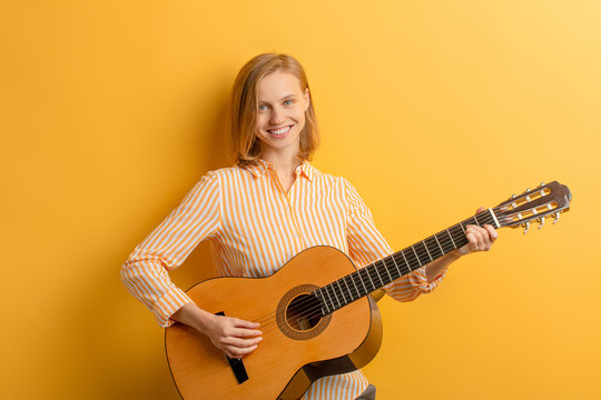 Portrait of young caucasian pretty musician woman in casual shirt. Young female artist guitarist. Cheerful woman with musical instrument isolated over yellow background