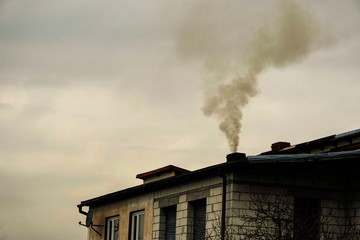 black smoke comes from chimney of a house against gray sky, heating with coal in winter....