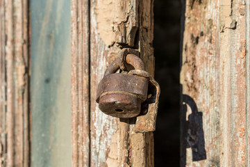 Old  rusty iron lock hanging on a broken door of an old building on the Newport street in the old part of Kutaisi in Georgia, in the morning sun