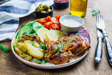 Lunch bowl with grilled chicken, red onion, tomato, cucumber, lemon, olive and sause on wooden background.
