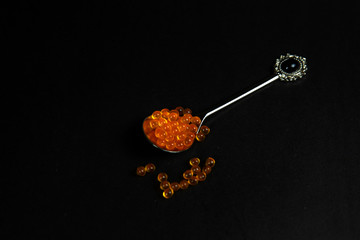 Red caviar in a spoon. Caviar in a bowl on a black background. Gourmet food.