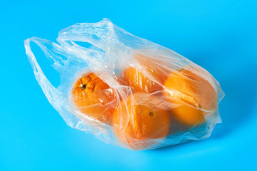 Fototapeta premium Fresh whole mandarins or oranges in polietilene bag on blue background. Fruit purchasing concept. Close-up