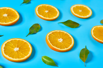 Naklejka na ściany i meble Scattered pieces of mandarin or orange and green leaves on blue background. Fruit purchasing concept. Close-up