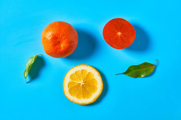 Scattered whole and pieces of mandarins or oranges, persimmon and green leaves on blue background. Fruit purchasing concept. Top view. Close-up