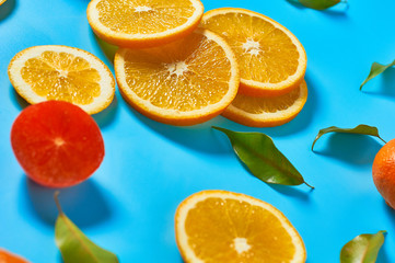 Scattered whole and pieces of mandarins or oranges, persimmon and green leaves on blue background. Fruit purchasing concept. Close-up