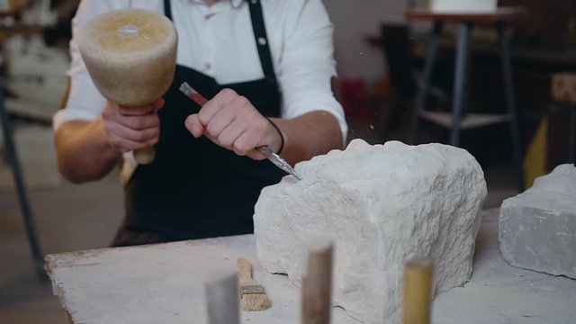 Front view of professional male hands which holding the mallet ans chisel knocking off the shape of future sculpture