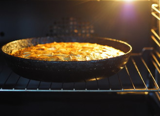 Homemade baking. Round apple pie in a black pan in the oven.