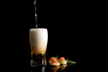 Beer poring with Caviar and bread on black background with reflections. Copy space