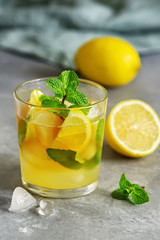 Cold refreshing tea with lemon, mint and ice in a glass on a gray concrete background. Summer drink. Selective focus.