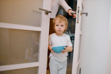Fototapeta na wymiar little caucasian boy, child stay near the door at home holding blue dish in hands, sweet child