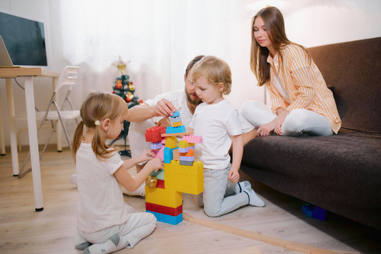 happy family concept. careful parents looking after children at home, cute little children playing with toys on the floor, while their young parents look after them and play together