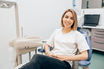Portrait of attractive caucasian woman sit in dentist office in casual wear, smiling, have ideal smile. Medical dental equipment in the background