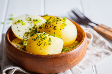 Boiled potatoes with greens in a wooden bowl, white background.