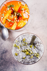 Chia pudding with persimmon and pumpkin seeds in glasses, gray background, top view. Vegan food concept.