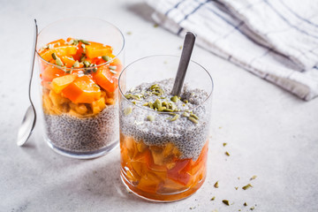 Chia pudding with persimmon and pumpkin seeds in glasses, gray background, copy space. Vegan food concept.