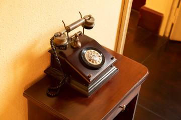 A classic Antique wooden telephone standing on a table against a yellow wall