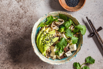 Buckwheat noodles - soba with tofu, broccoli, avocado, seedlings and cilantro, top view, copy space. Healthy vegan food concept.