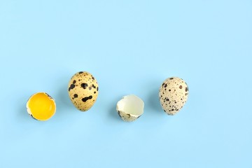 Broken quail eggs with yellow yolk on neutral light blue background. Raw organic quail egg. Easter eggs. Ingredients for healthy protein breakfast. Keto diet. Easter background traditional symbol 