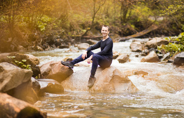Traveler man wearing in black sitting on rock in mountain river between forest.
