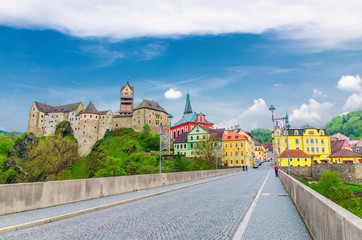 Loket Castle Hrad Loket gothic style building on massive rock, colorful buildings in town, bridge over Eger river, blue cloudy sky background, Karlovy Vary Region, West Bohemia, Czech Republic