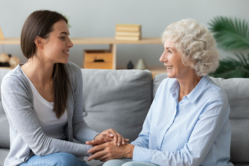 Happy grandmother and granddaughter chatting at home, holding hands