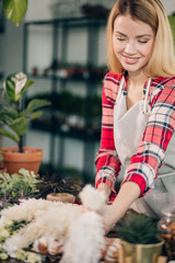 young attractive gardener at work, take care of green plants, enjoy working with flowers, isolated in room full of flowers and plants, botany concept
