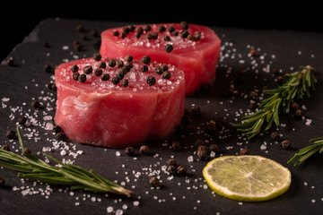 Fresh raw tuna fillet for steak on cutting board with lemon lime salt pepper and spices on dark black rustic background. Tasty fish dinner. Ingredients for cooking