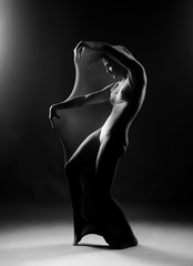 Slim girl wearing a white bodysuit dances a modern avant garde dance, covering her body with elastic transparent fabric. Artistic, conceptual, monochrome and creative design. Silhouette  photography.