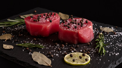 Fototapeta na wymiar Fresh raw tuna fillet for steak on cutting board with lemon lime salt pepper and spices on dark black rustic background. Tasty fish dinner. Ingredients for cooking