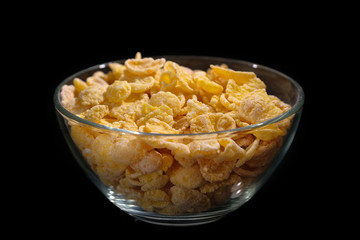 A bowl of cornflakes isolated on a black background.