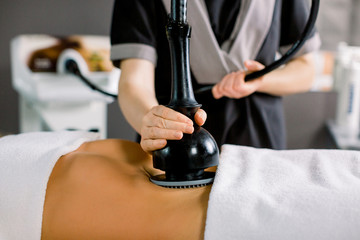 Lymphatic drainage massage device, anti cellulite body correction. Cropped image of woman client receiving vacuum massage of the abdomen and hands of female doctor holding the device