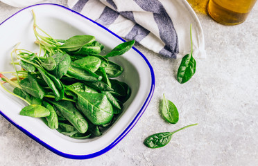 Fresh green baby spinach on plate on stone table. Healthy diet, vegetarian food concept.