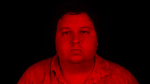 Portrait shot with red lighting: Fat man standing isolated on black background and looking at camera