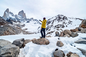 Fototapeta premium A hiker with a yellow jacket taking a photo on the base of Fitz Roy Mountain in Patagonia, Argentina