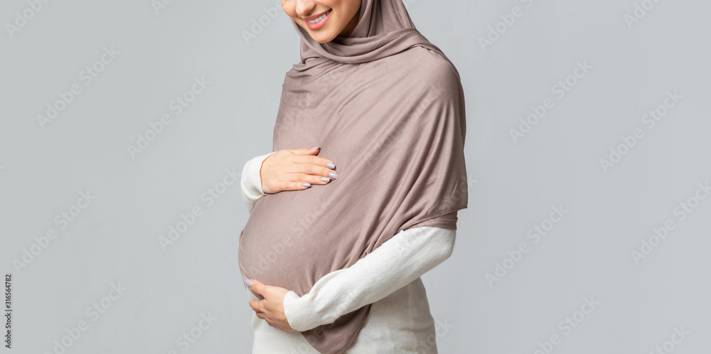 Wall mural unrecognizable pregnant islamic woman in hijab touching her belly