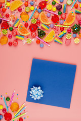 Flat lay view at sweet background of greeting card and different type color and taste candies and birthday candles on pink