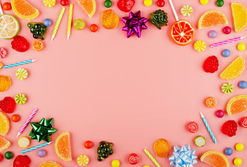 Flat lay view at sweetframe of different type color and taste candies and birthday candles on pink. Space for text