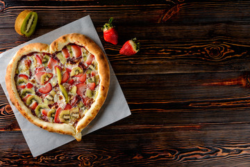 heart-shaped strawberry and kiwi pizza cake on a wooden table