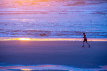 France.  Somme. un coureur à pied court le long de la mer sur la plage au coucher de soleil. a...