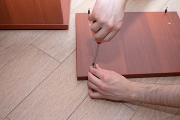 Fototapeta na wymiar A male tool collects furniture color spanish walnut. A screwdriver screws the screws to the wooden wall of the table.