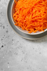 Grated carrots with honey in a gray bowl on a gray kitchen table. Food for vegetarians