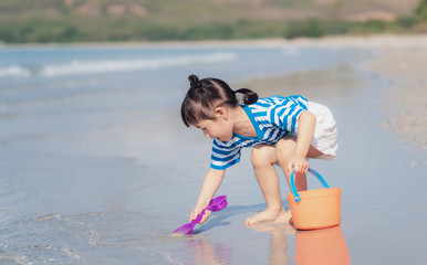 Little asian baby girl playing sand on the beach. Kid three years old play with sand toys.