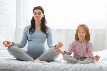 Pregnant mother and little daughter doing yoga together