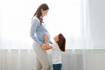 Excited little girl touching pregnant mom tummy