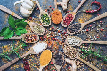 Colourful various herbs and spices in spoons for cooking on dark background