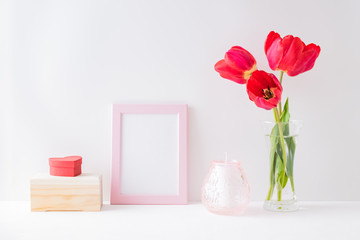 Home interior with decor elements. Mockup with a pink frame, red tulips in a vase on a light background