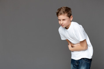 Teen boy suffering from stomachache, grey background