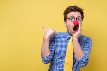 Shocked man with red clown nose looking camera showing pointing on copyspace. Clown, corcus or show...