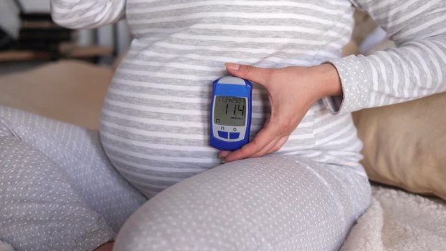 Pregnant woman showing glucose meter with result of measurement sugar level, concept of diabetes during pregnancy, expecting for newborn. High blood sugar in a pregnant woman.